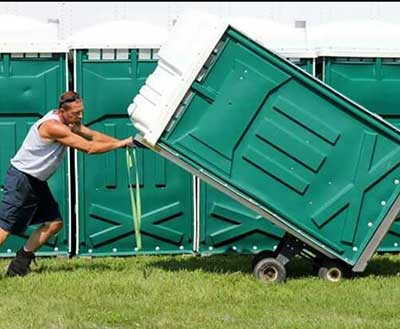 guy pushing a large port a potty through a field.